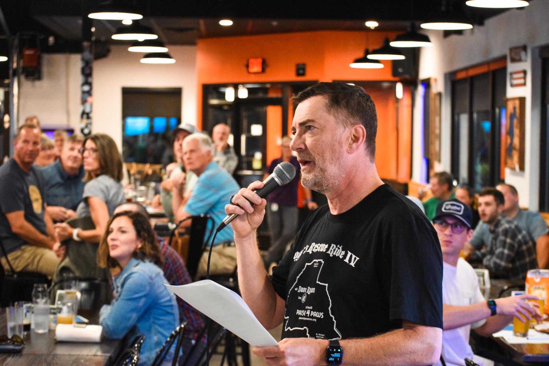 Photo of environmental trivia players at Chanhassen Brewing Company. Radio host Dave Ryan guest hosts, talking into a microphone.